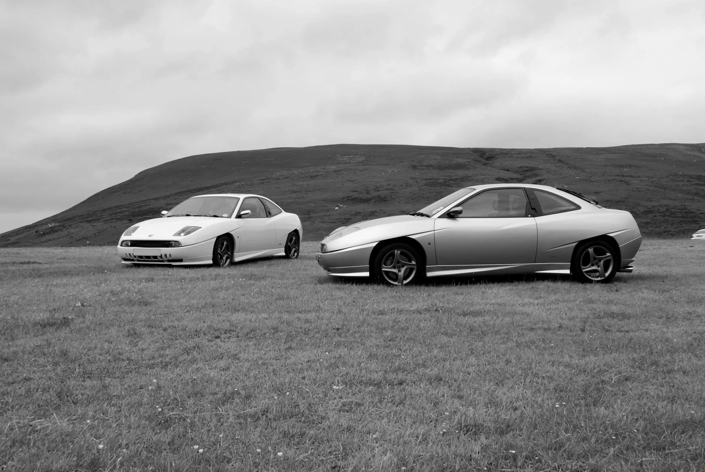 Two Fiat Coupés parked on the hillside